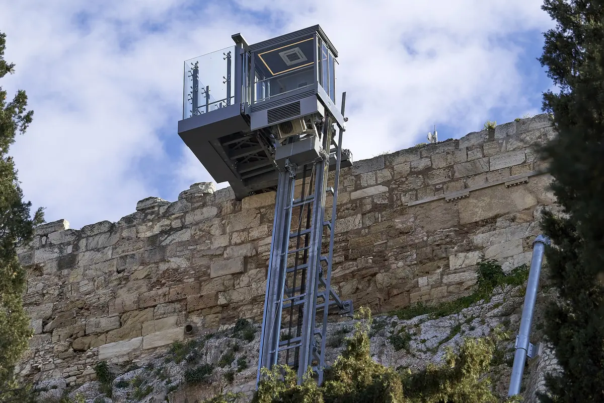 En elevator med glasfront i et ståltårn op ad en støttemur på Akropolis