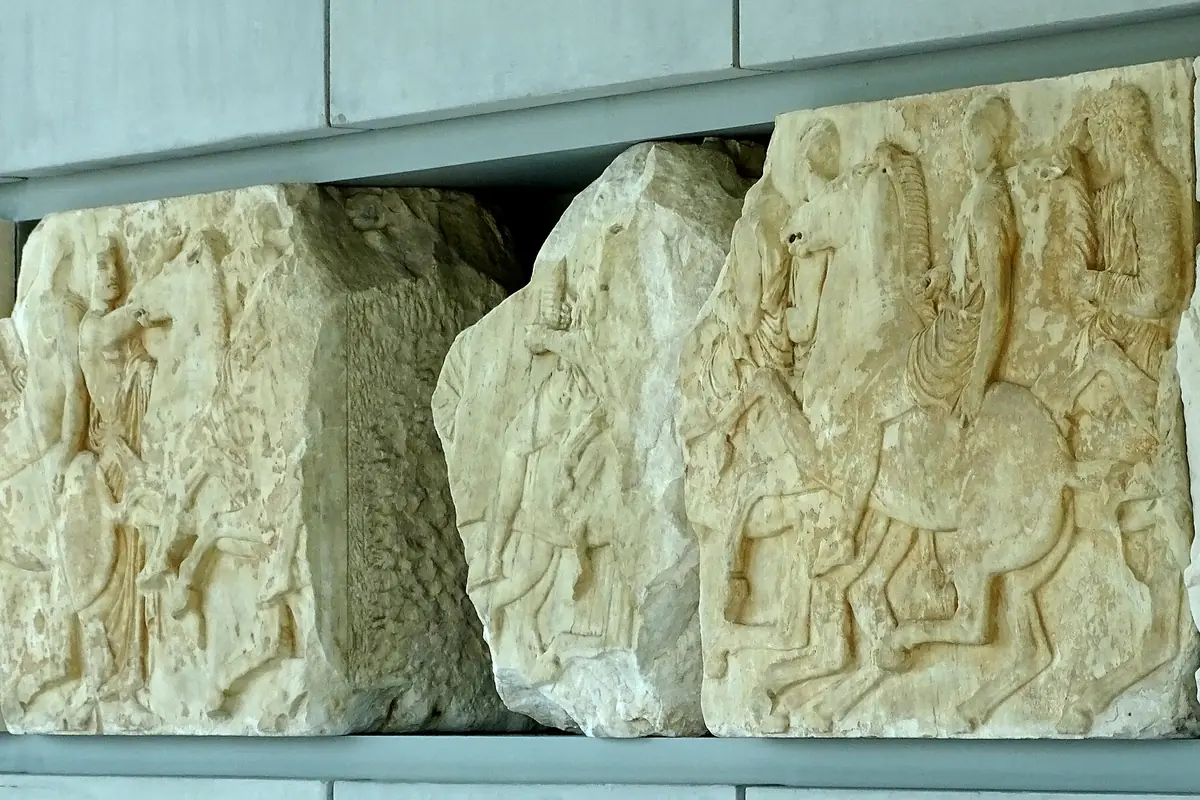 Mramorové bloky z Parthenonského vlysu zobrazující jezdce, vystavené v muzejní síni.
